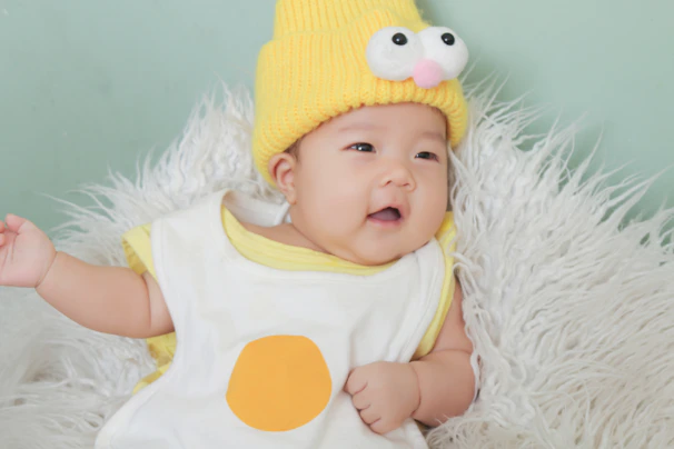 Close-up of a stylish baby wearing a soft onesie and a playful knit hat against a cheerful backdrop