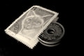 A vintage postage stamp featuring a cat is positioned next to an old coin with a hole in the center. Both items are displayed against a dark background, highlighting their details. The stamp has Bulgarian text and a numeric value, while the coin displays symbols and characters.