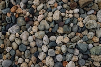 A collection of smooth river stones in varying shades of gray and brown, arranged artfully on a wooden surface.