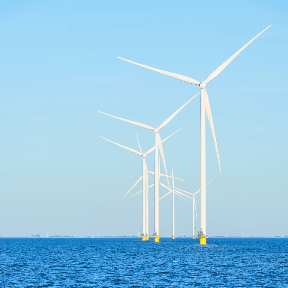 Four wind turbines stand tall on the ocean's surface with white blades angled towards right