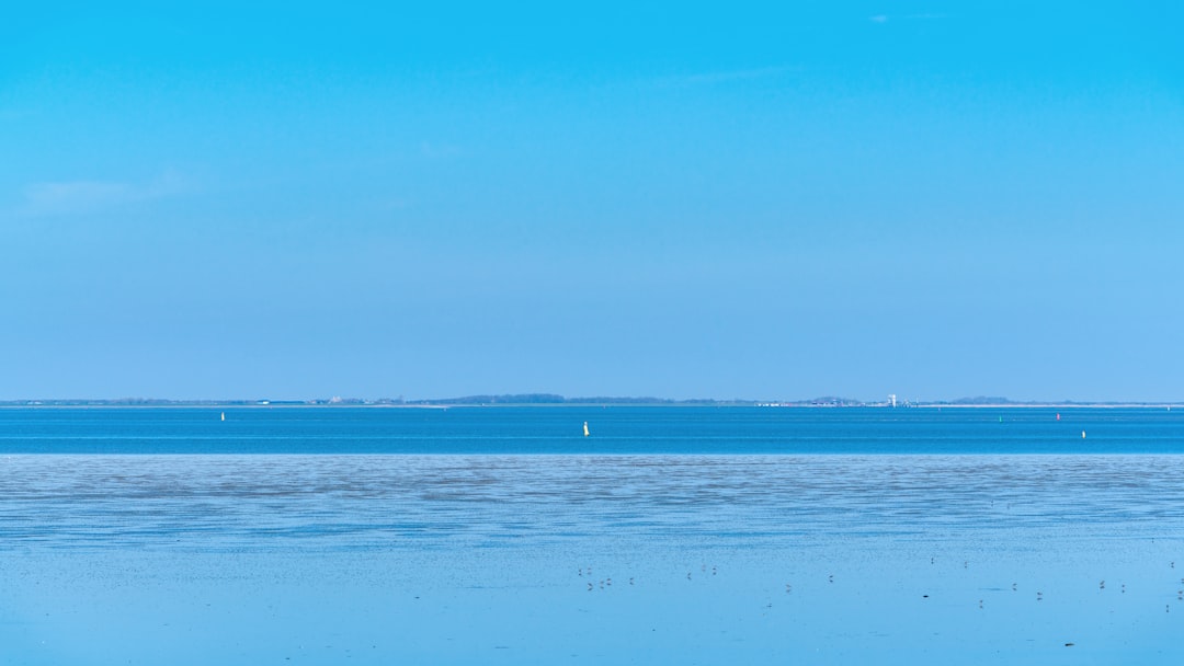 a body of water with snow on the ground and blue sky, Netherlands - April 2022: north sea coast