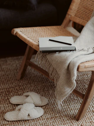 Softly lit cozy corner with a warm blanket, a steaming cup of tea, and a journal resting on a cream-colored armchair.