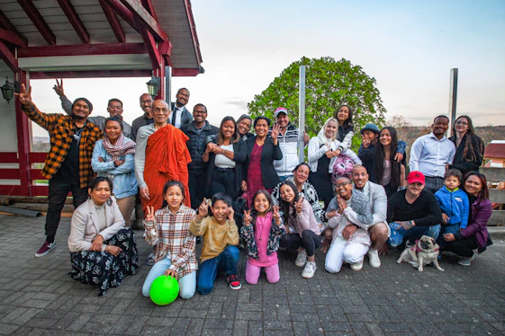 A diverse group of people holding hands in a circle outdoors, smiling warmly under a clear sky.