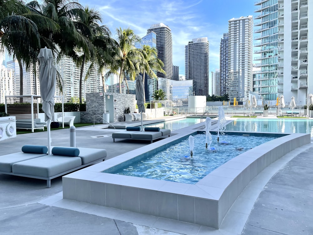 a pool with a fountain in it and buildings in the background