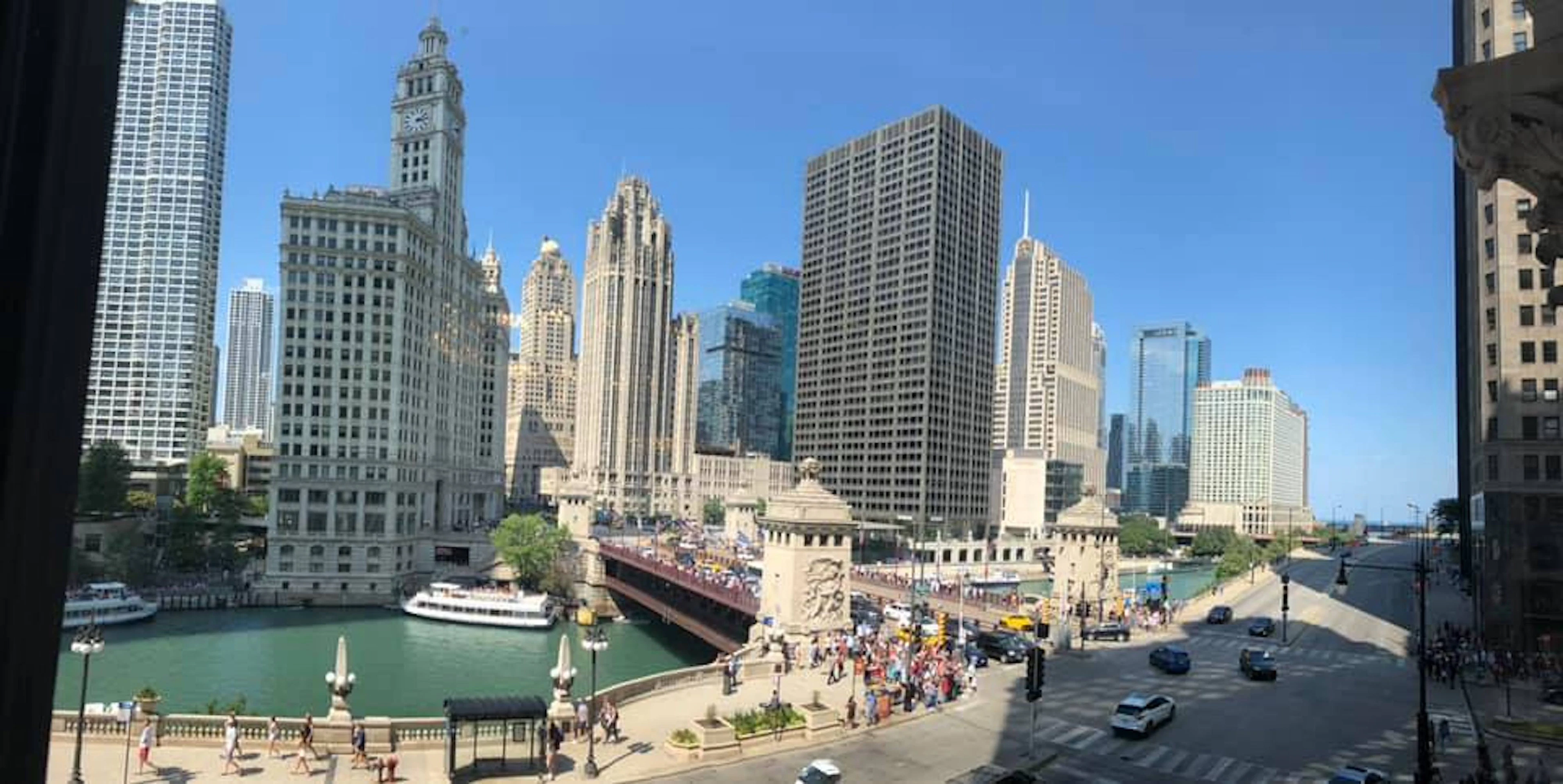 The Wrigley Building and DuSable Bridge rise over the Chicago River on a bright, busy afternoon.