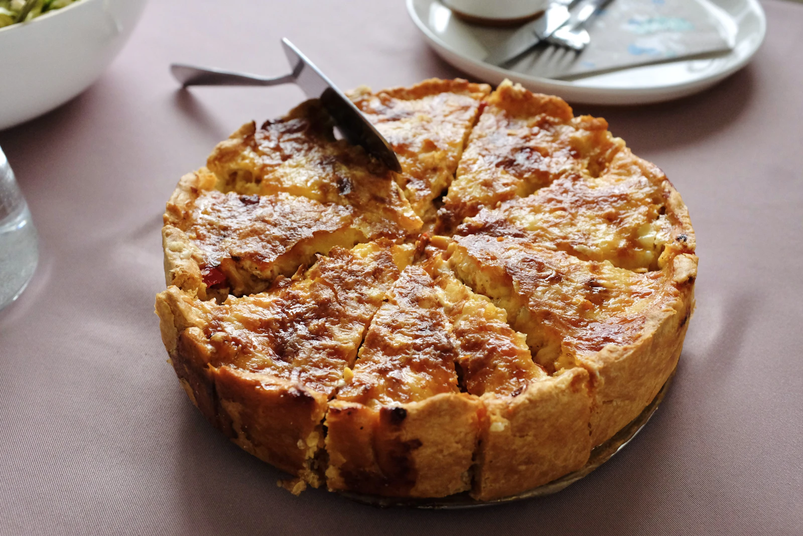 Quiche dorée coupée en parts, servie à table avec une salade