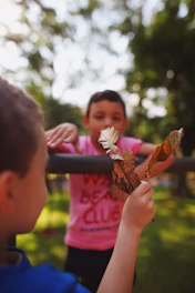 A candid shot of children joyfully examining leaves and insects in a sunlit garden.