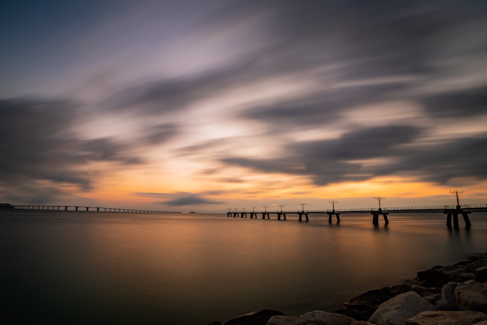 a body of water with a bridge and a sunset in the background