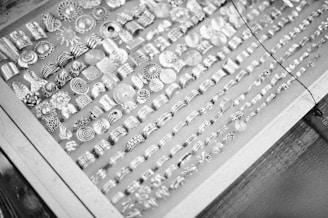 A display case filled with an array of intricately designed silver rings, each featuring different patterns such as spirals, floral motifs, and geometric shapes, arranged in multiple rows.