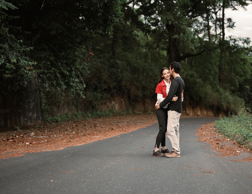 a man and woman kissing on a road with trees on either side