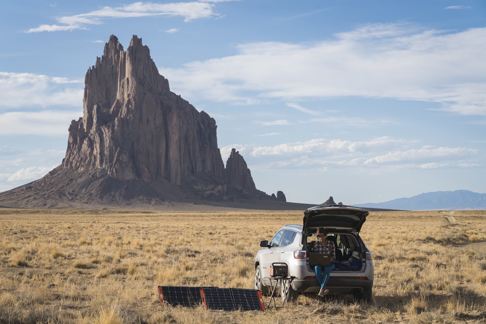 Un coche con el maletero abierto frente a una gran roca