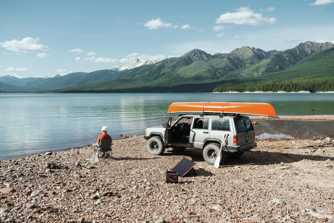 A camper using a portable power station beside a truck on a rocky shore