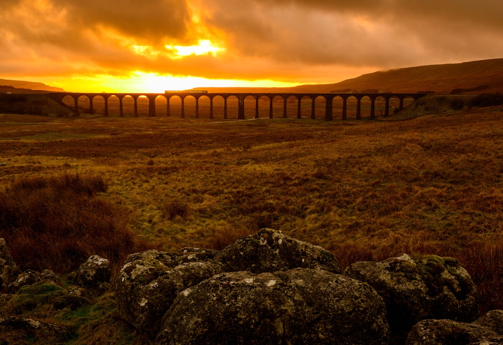 a large field with rocks and a sunset in the background