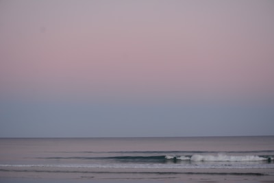 A peaceful ocean shore with waves softly rolling onto smooth stones under a pastel sky.