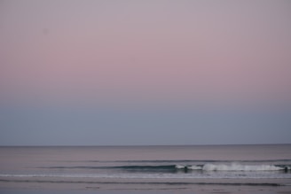 A peaceful ocean shore with waves softly rolling onto smooth stones under a pastel sky.