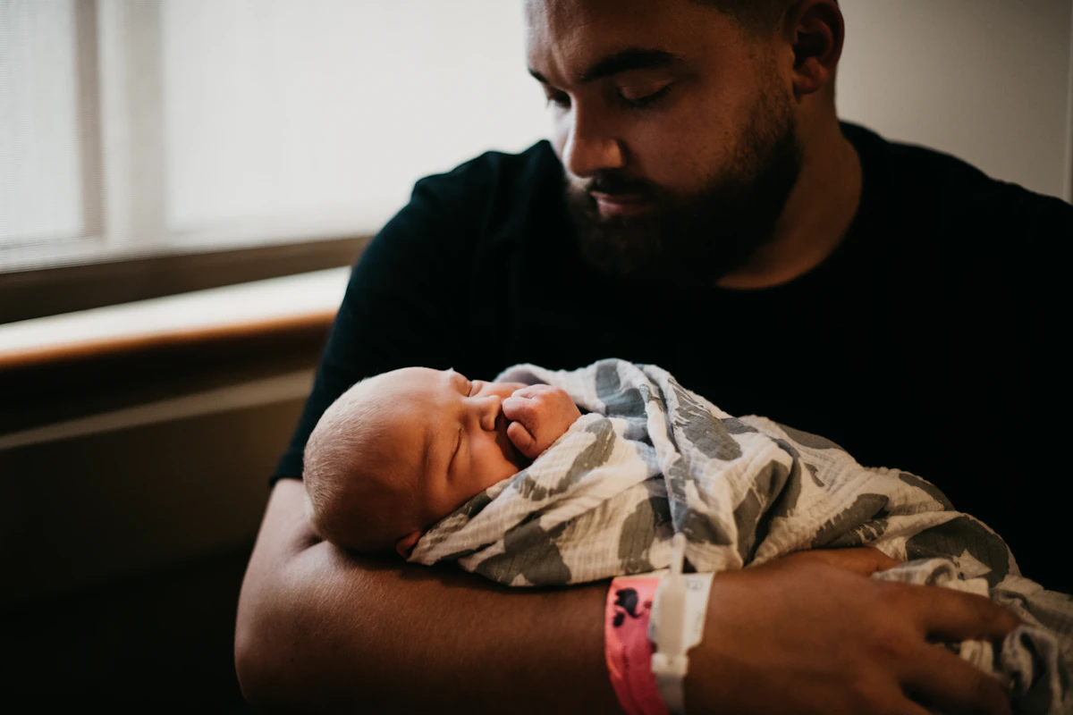 Father in a white t-shirt cradling his newborn son close, illustrating the fertility decisions men face when starting testosterone replacement therapy.