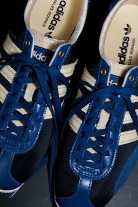 A pair of stylish adidas sneakers featuring deep blue leather with contrasting white stripes and laces. The interior insoles prominently display the adidas logo along with another branding, exuding a sense of modern fashion and sports style.