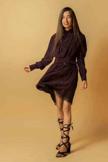 Model wearing a sleek black dress from dresply’s sale collection, standing against a soft beige backdrop