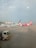 Two airplanes are parked on the tarmac of an airport. One airplane features a predominantly pink color with the AirAsia logo visible. The background includes airport buildings and infrastructure, with a clear blue sky overhead. A maintenance truck is positioned in the foreground beside the airplane.