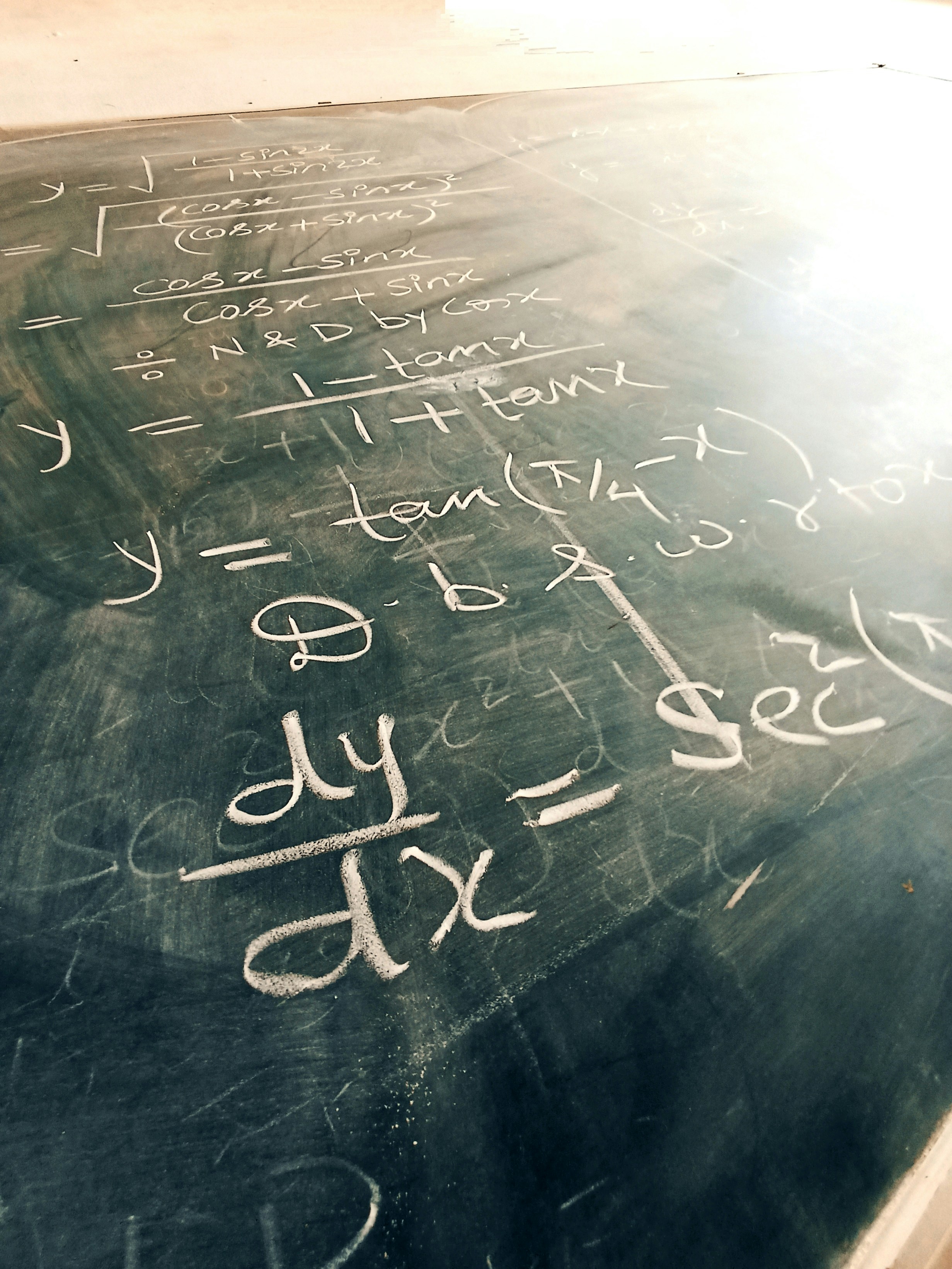 Calculus derivative equations on dark chalkboard, dim atmospheric classroom, deep shadows