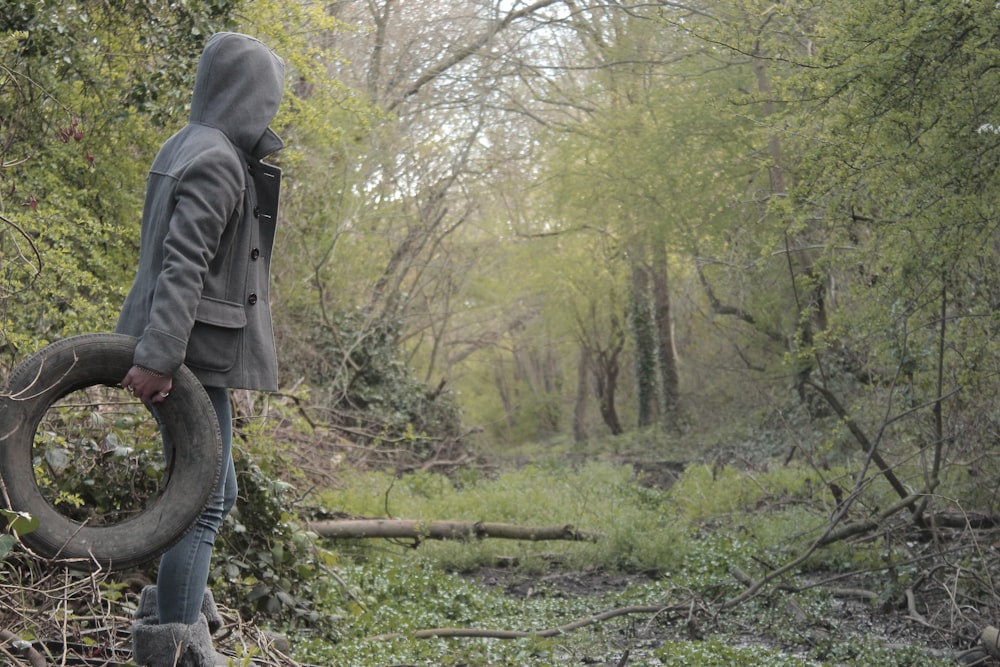 a person with a hood on a tree stump in a forest