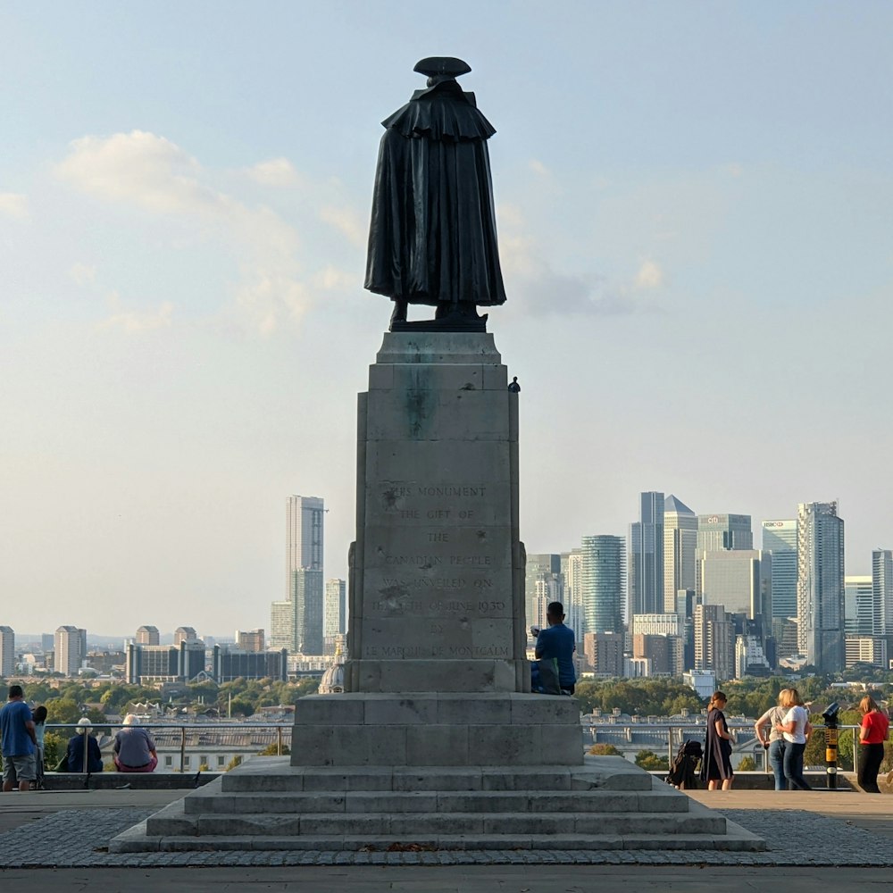 a statue of a person with a hat and a beard on a pedestal with a city in the