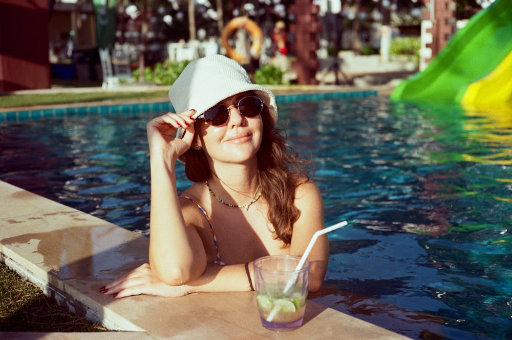 a woman in a hat and sunglasses sitting in a pool