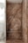 A luxurious bathroom shower area featuring elegant stone walls and floors with pronounced natural patterns. The walls have a rich, earthy appearance with dark and light brown streaks. Within the shower, several modern bottles and a brush are neatly placed on a shelf. The showerhead and controls appear sleek and contemporary. Adjacent to the shower is a glimpse of a toilet with a textured wall and frosted glass door.
