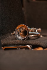 A shiny brass trumpet is resting on a dark, textured surface, likely a seat in a concert hall. The instrument's bell is prominently visible, reflecting the warm ambient light.
