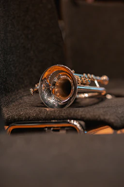 A close-up of a shiny brass trumpet resting on sheet music with soft natural light.