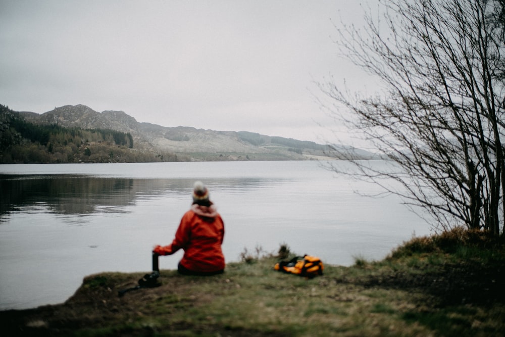 a man sitting on a hill by a lake with a fire extinguisher