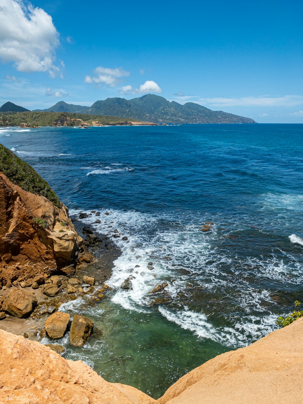 a rocky beach with a body of water and mountains in the background