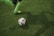 A close-up of soccer shoes kicking a ball on a grassy pitch.