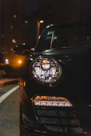 Close-up of a sleek car headlight glowing bright white at night on a city street.