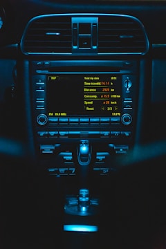 An illuminated car dashboard with detailed trip data displayed on the screen. Buttons and controls are visible below the screen, all bathed in a blue light.