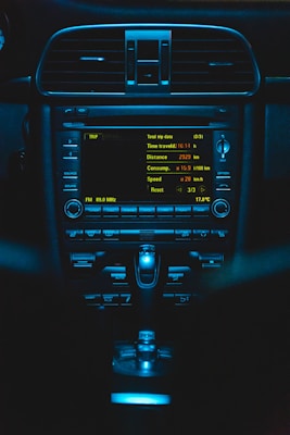 An illuminated car dashboard with detailed trip data displayed on the screen. Buttons and controls are visible below the screen, all bathed in a blue light.