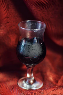 Close-up of a chilled glass of gosattuu with condensation, surrounded by roasted chickpeas and fresh green leaves on a rustic wooden table.