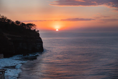 A serene coastal cliffside with waves crashing against rugged rocks at sunset.
