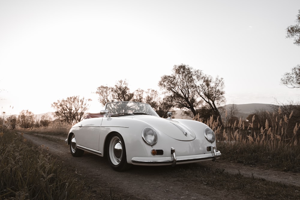 a white car parked on a dirt road with trees and hills in the background