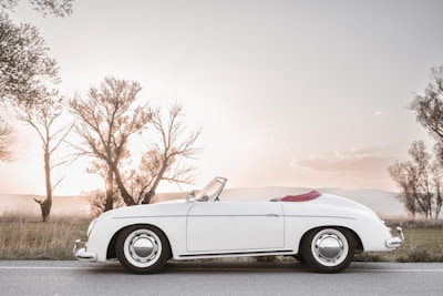 A white convertible car parked near a scenic coastal road at sunset.