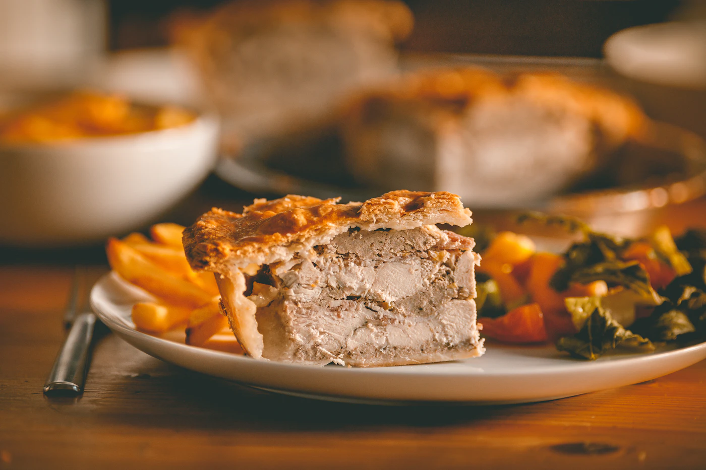 Thick slice of double-crust chicken pie showing large chicken pieces beneath a deeply golden flaky pastry top
