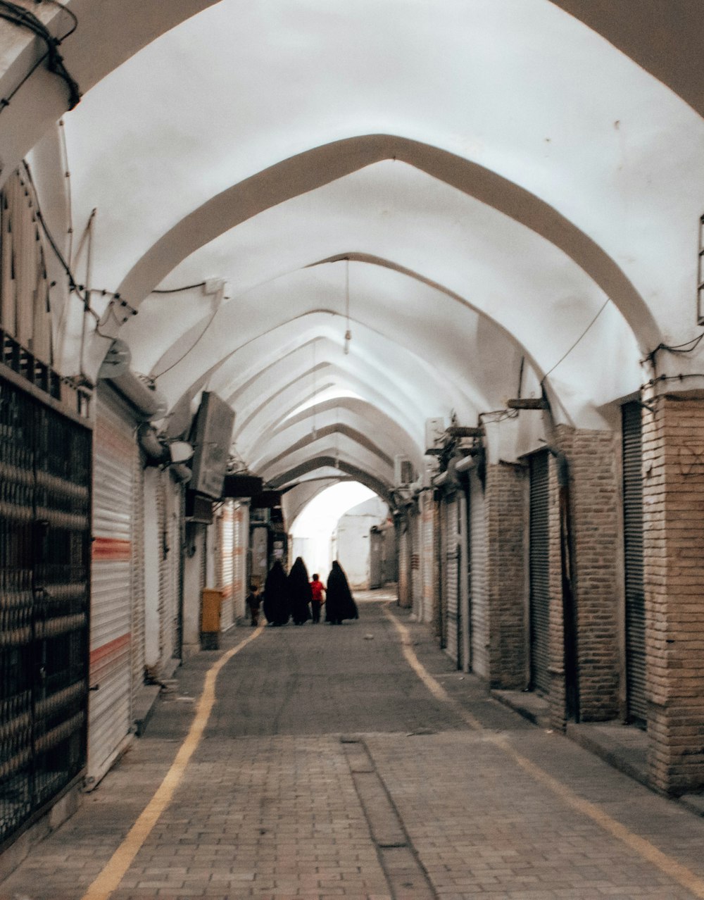 a group of people walking down a walkway between brick walls