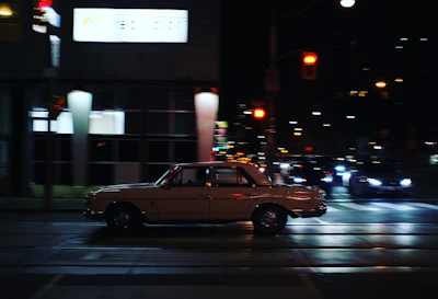 A vintage convertible from the 1990s cruising a moonlit city street with stars overhead.