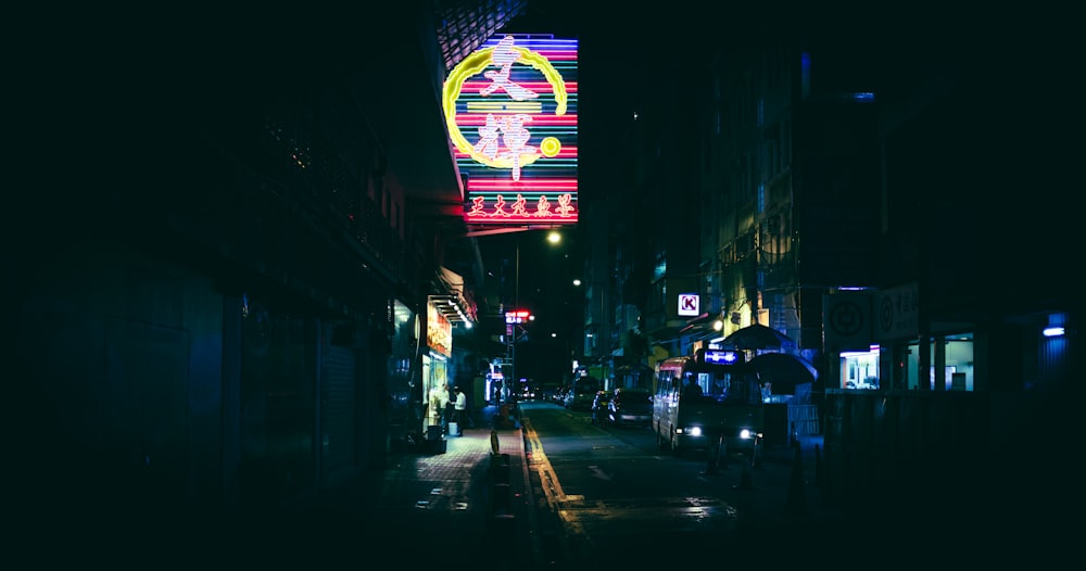 a street with cars and buildings with neon signs at night