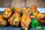 Golden brown chicken wings glazed with a sauce, garnished with fresh cilantro and sesame seeds, presented on a dark gray slate surface.