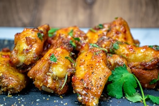 Golden brown chicken wings glazed with a sauce, garnished with fresh cilantro and sesame seeds, presented on a dark gray slate surface.