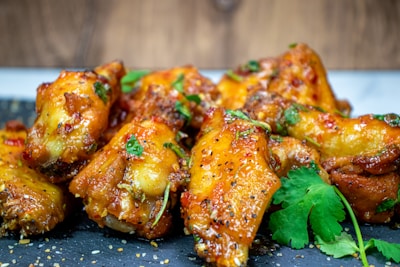Golden brown chicken wings glazed with a sauce, garnished with fresh cilantro and sesame seeds, presented on a dark gray slate surface.