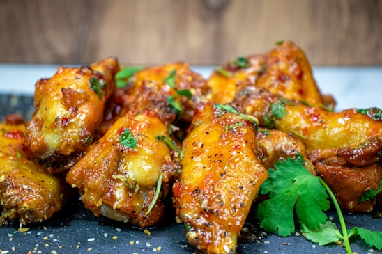 Golden brown chicken wings glazed with a sauce, garnished with fresh cilantro and sesame seeds, presented on a dark gray slate surface.