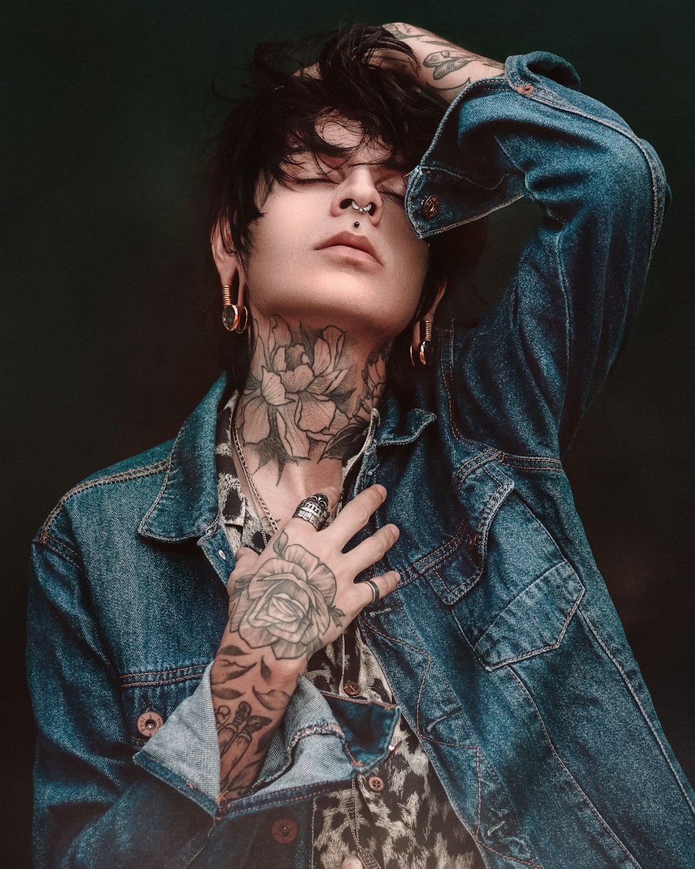 a person with tattoos and a blue jacket with a black background