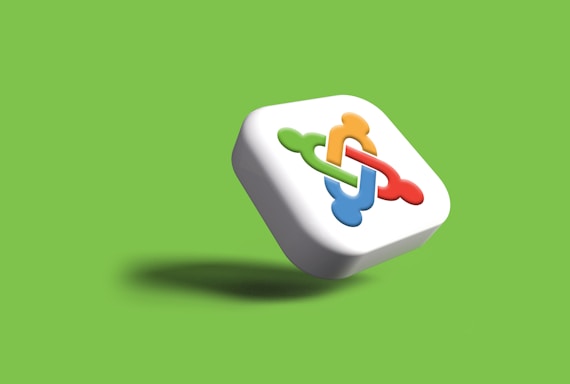 A three-dimensional square with rounded edges featuring an interlocking design in red, green, blue, and orange on its front, set against a vibrant green background. The shadow underneath suggests the object is floating.